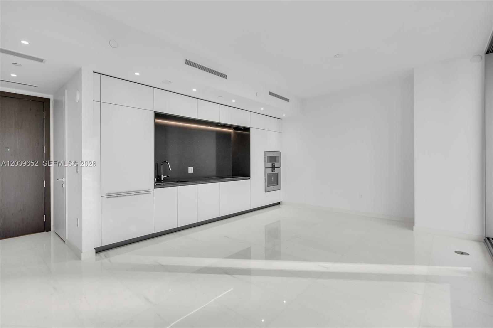 A minimalist kitchen features white cabinetry, a dark recessed backsplash, and polished white flooring — 300 Biscayne Blvd Way # 4008, Miami FL 33131, MIAMI, FL