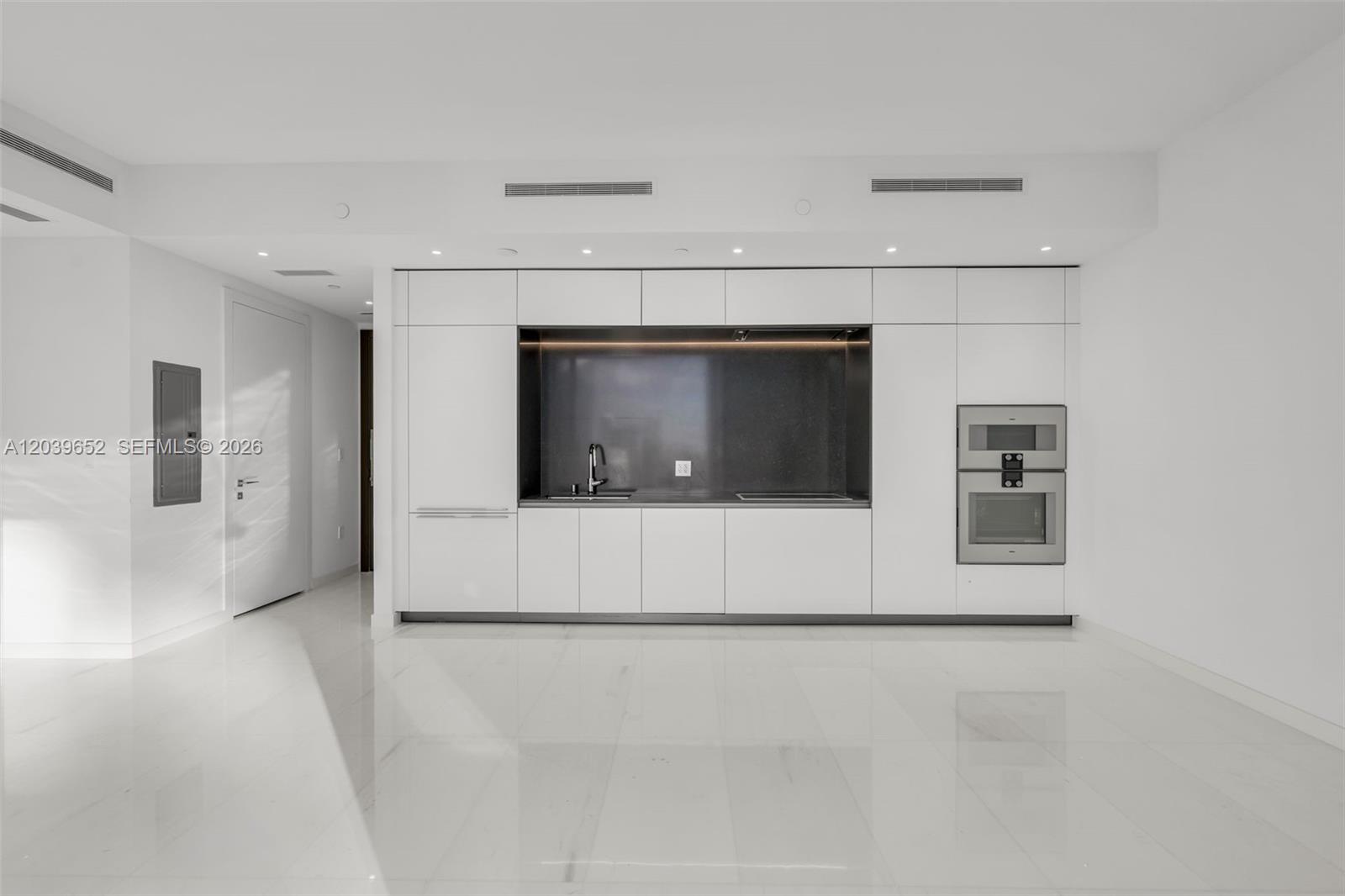 A modern, minimalist kitchen features white cabinetry, a dark backsplash, and polished white flooring — 300 Biscayne Blvd Way # 4008, Miami FL 33131, MIAMI, FL