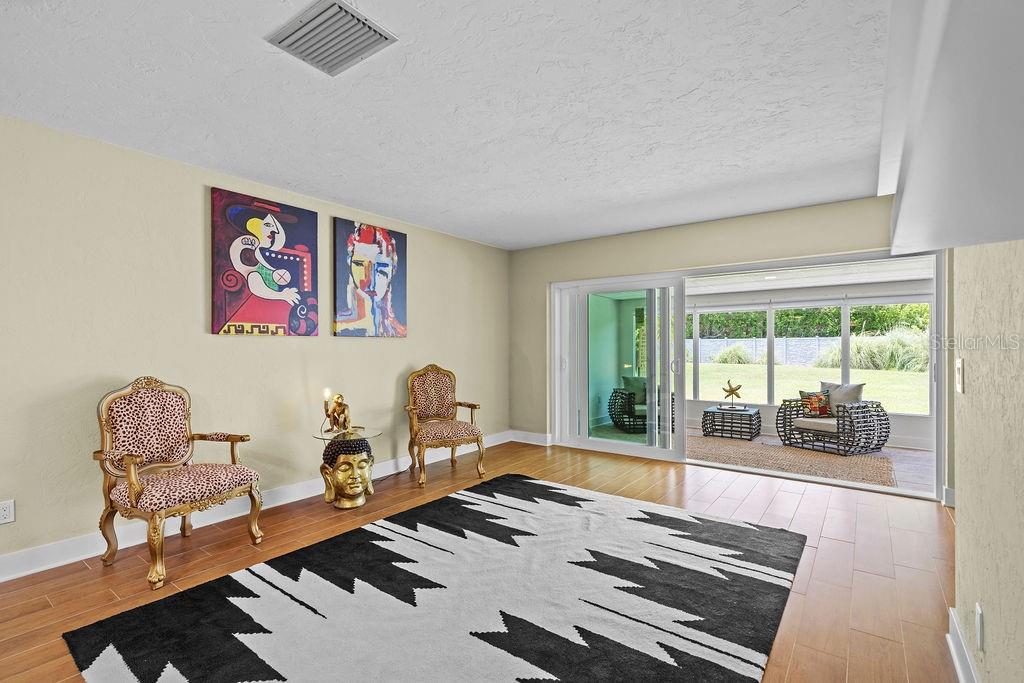 A living room features hardwood floors, a patterned area rug, two chairs, and sliding glass doors — 215 BOCA CIEGA POINT BOULEVARD N UNIT 3, ST PETERSBURG, FL
