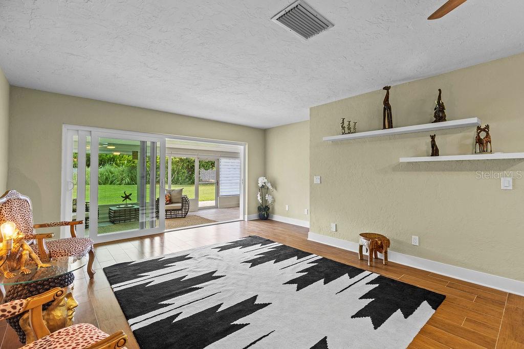 A living room with light green walls, wood flooring, a patterned rug, and sliding glass doors — 215 BOCA CIEGA POINT BOULEVARD N UNIT 3, ST PETERSBURG, FL