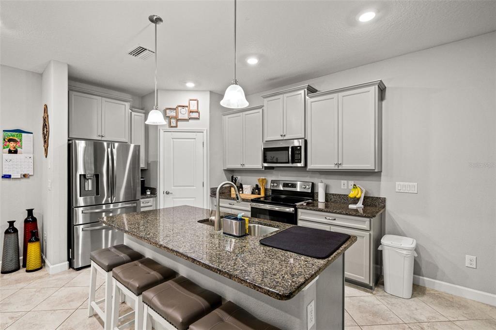 A kitchen features light gray cabinets, granite countertops, a center island, and stainless steel appliances — 6612 CITRUS CREEK LANE, TAMPA, FL
