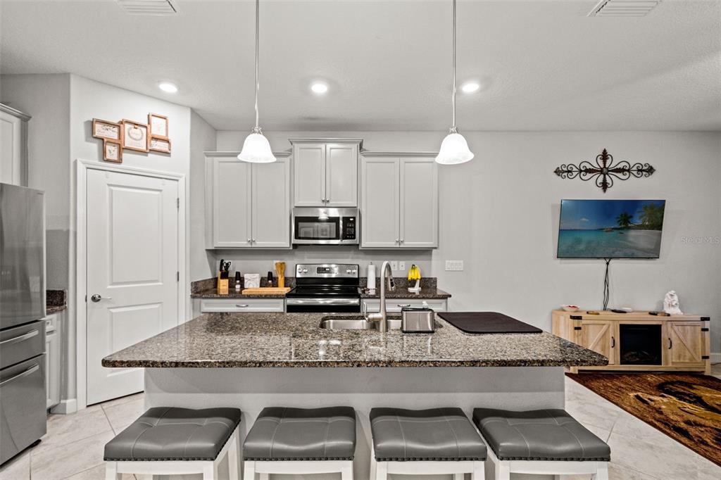 A kitchen features a granite-topped island with four stools, light gray cabinets, and stainless appliances — 6612 CITRUS CREEK LANE, TAMPA, FL