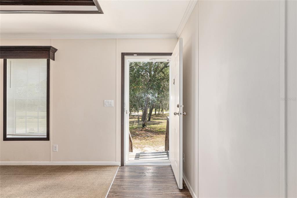 An interior view shows a carpeted living area leading to an open door revealing trees — 14671 SE 5TH PLACE, WILLISTON, FL