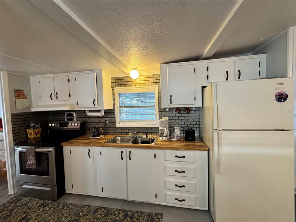 A kitchen features white cabinets, a wood countertop, a subway tile backsplash, and white appliances — 1710 7TH STREET SW UNIT 2, RUSKIN, FL
