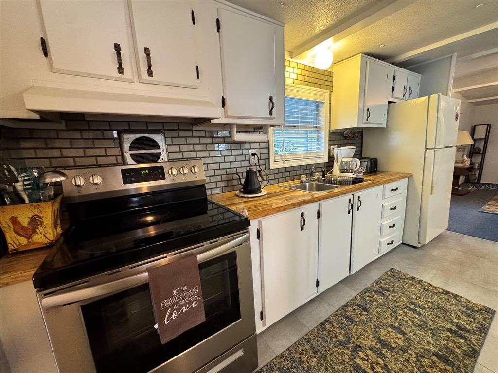 A kitchen features white cabinets, a stainless steel stove, and wood countertops with a backsplash — 1710 7TH STREET SW UNIT 2, RUSKIN, FL
