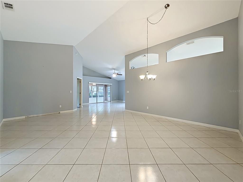 A spacious, open-concept living area features light gray walls, white tile flooring, and vaulted ceilings — 3811 WESTERHAM DRIVE, CLERMONT, FL