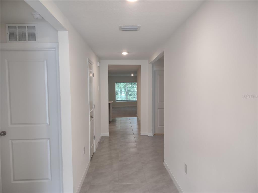 A hallway with light-colored tile flooring leads toward a room with a large window — 5215 BYRONIC COURT, BROOKSVILLE, FL