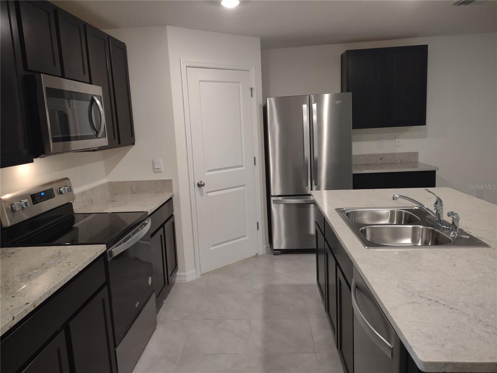 A kitchen features dark cabinets, stainless steel appliances, a center island, and light-colored countertops — 5215 BYRONIC COURT, BROOKSVILLE, FL