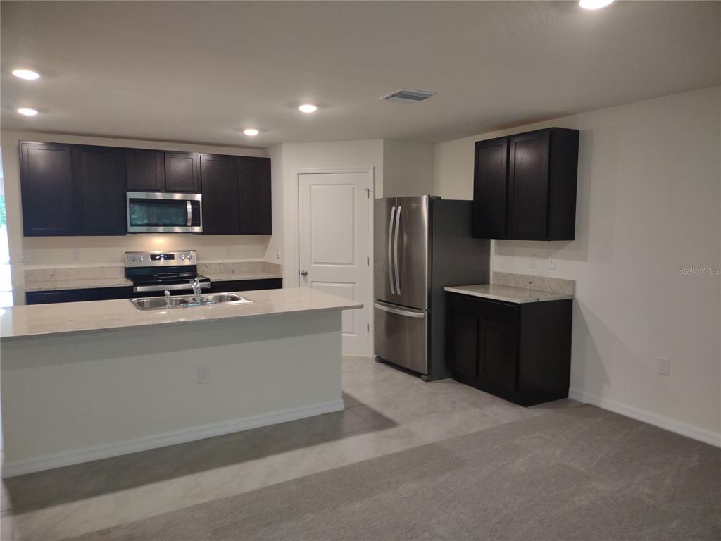 A kitchen features dark wood cabinets, stainless steel appliances, and a light-colored quartz island — 5215 BYRONIC COURT, BROOKSVILLE, FL