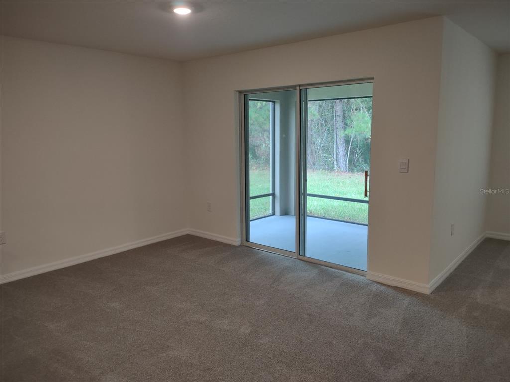 An empty room with beige carpet, white walls, and a sliding glass door to a patio — 5215 BYRONIC COURT, BROOKSVILLE, FL