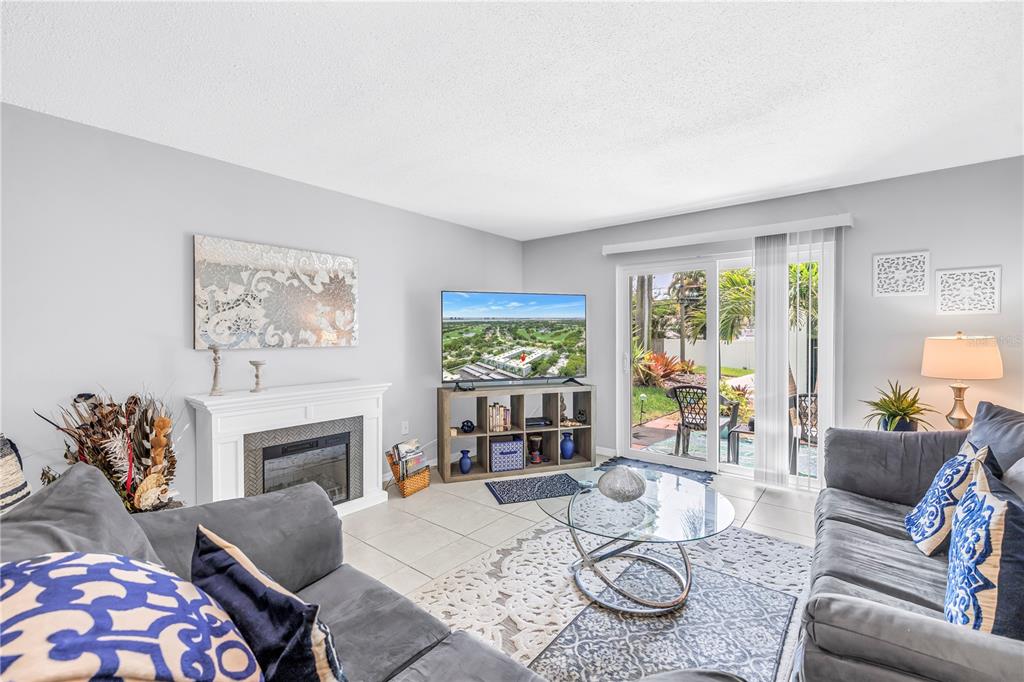 A living room features a fireplace, a television on a stand, and sliding glass doors — 701 POINSETTIA ROAD UNIT 116, BELLEAIR, FL