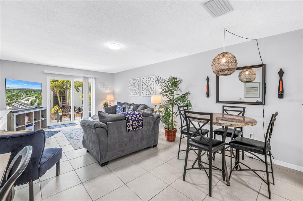 A living and dining area with tile floors, a gray sofa, and a patio door — 701 POINSETTIA ROAD UNIT 116, BELLEAIR, FL
