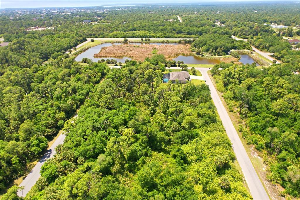 An aerial view shows a house surrounded by dense forest and a large retention pond — 18079 EBER AVENUE, PORT CHARLOTTE, FL