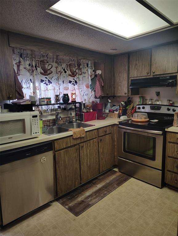 A kitchen features wood-grain cabinets, stainless steel appliances, a double sink, and patterned window curtains — 2962 MORGAN COMBEE ROAD, LAKELAND, FL