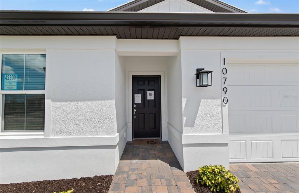 The exterior of a white stucco house features a black front door and garage door — 10790 BUTTERCUP COURT, VENICE, FL