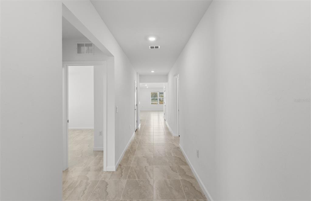 A long hallway with light-colored tile flooring leads toward a bright, open living space — 10790 BUTTERCUP COURT, VENICE, FL