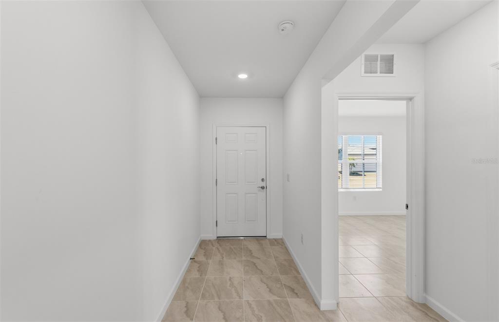 A bright entryway features white walls, a white front door, and light-colored tile flooring — 10790 BUTTERCUP COURT, VENICE, FL