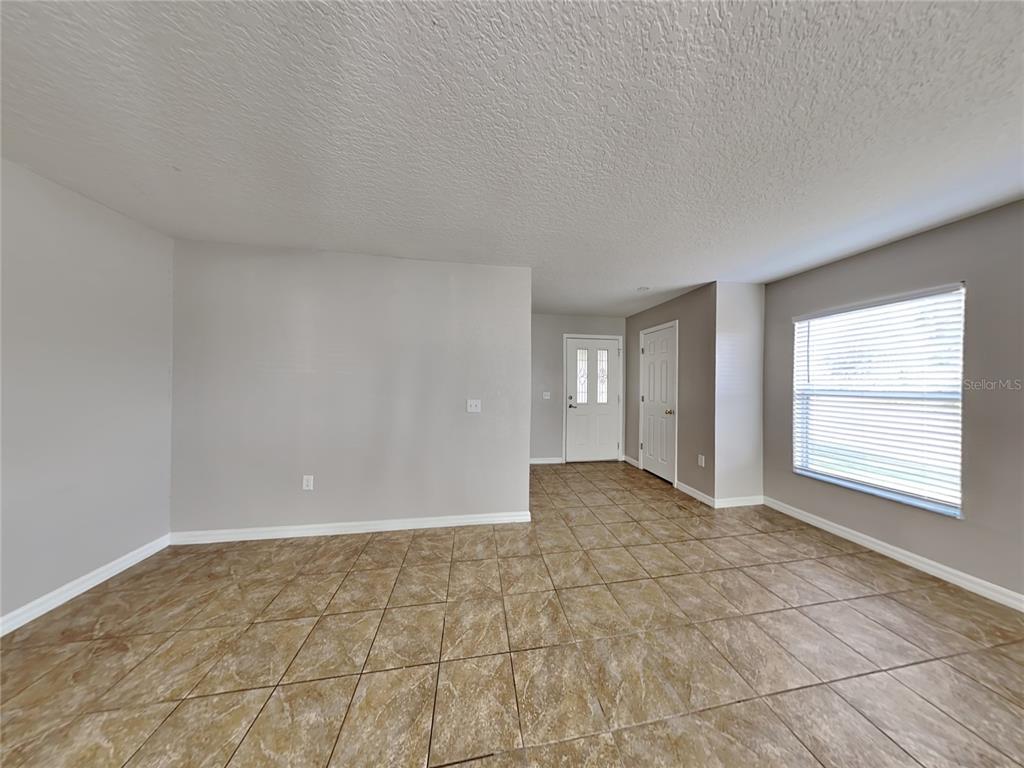 An empty room with light gray walls, tile flooring, a front door, and a window — 1388 N PLATTE COURT, KISSIMMEE, FL
