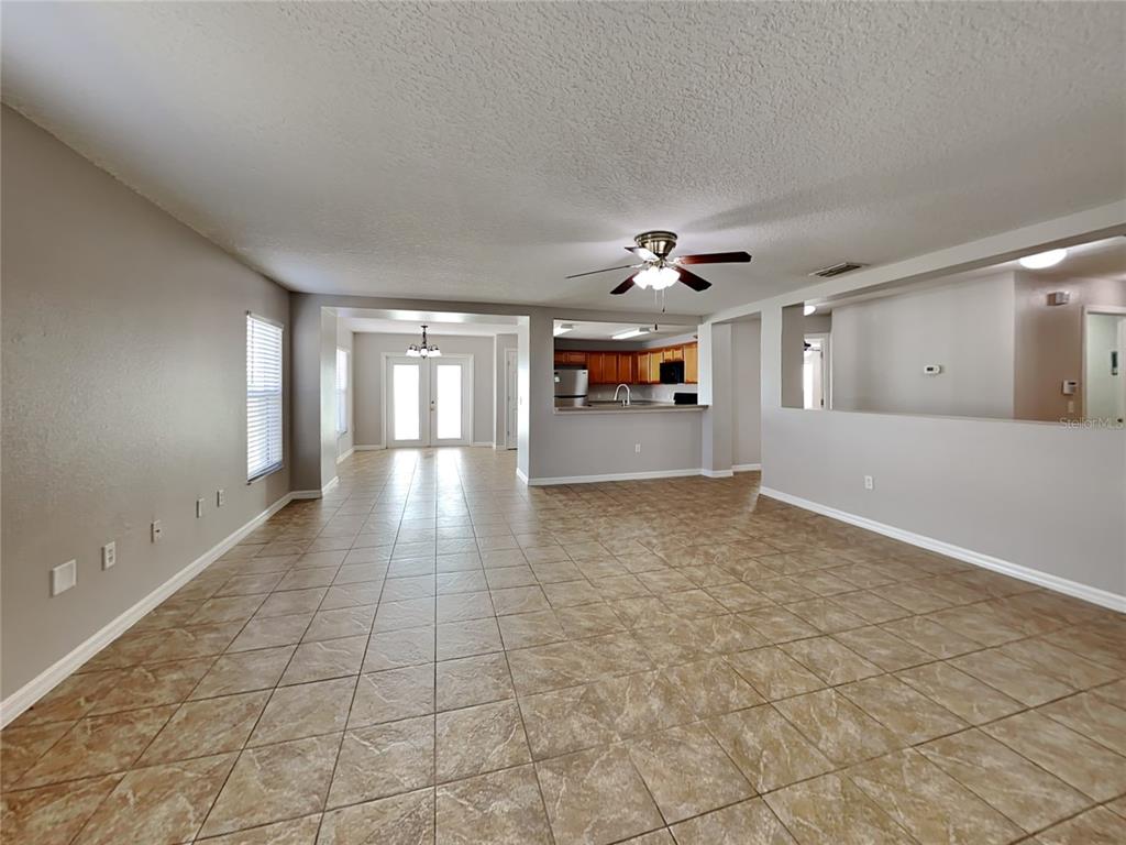 A spacious living area with tan tile flooring, a ceiling fan, and an open kitchen — 1388 N PLATTE COURT, KISSIMMEE, FL