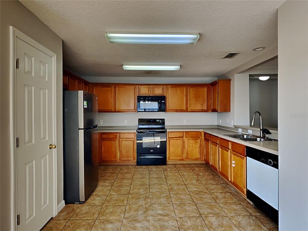 A kitchen features wood cabinets, black appliances, tile flooring, and two overhead fluorescent lights — 1388 N PLATTE COURT, KISSIMMEE, FL
