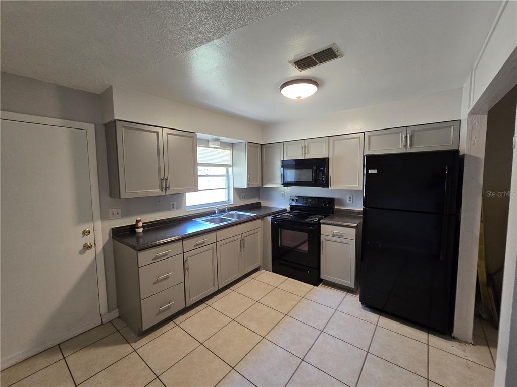 A kitchen features gray cabinets, dark countertops, black appliances, and light-colored tile flooring — 5667 STRUTHERS COURT, WINTER HAVEN, FL