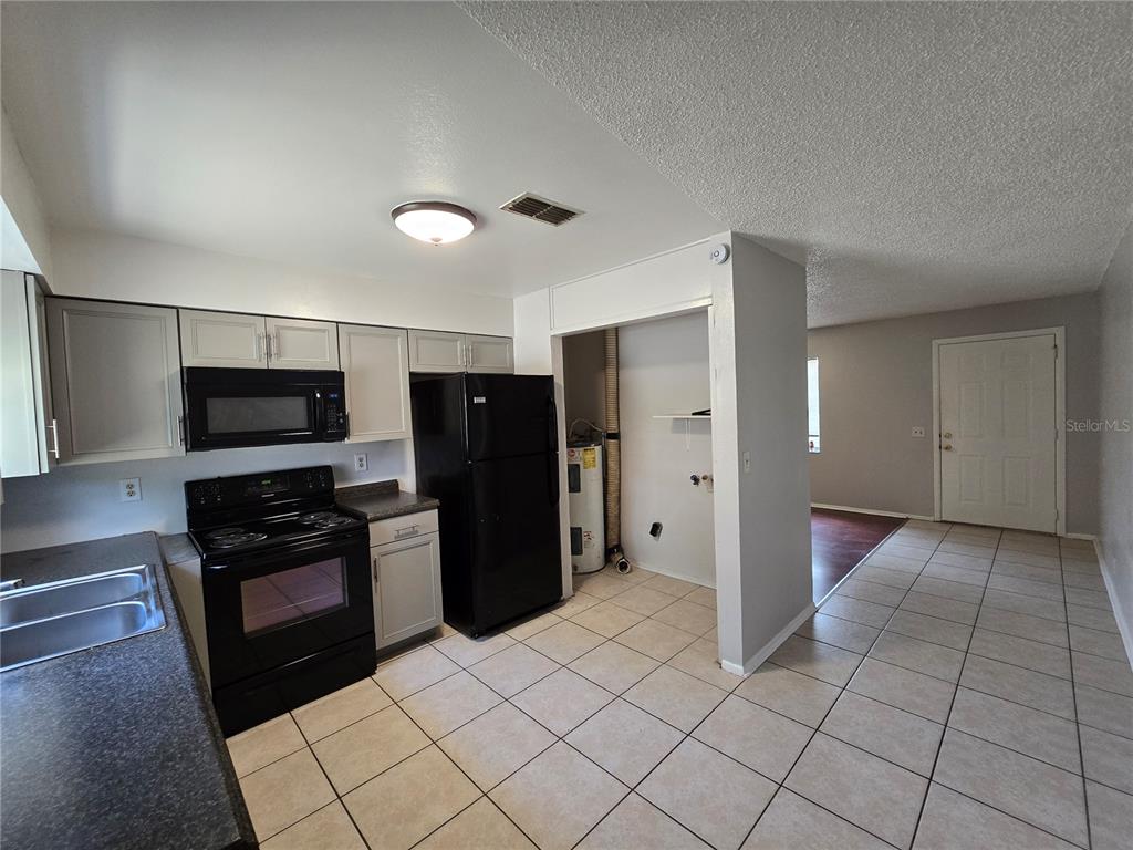 A kitchen with light cabinets, black appliances, tile flooring, and an adjacent utility closet — 5667 STRUTHERS COURT, WINTER HAVEN, FL