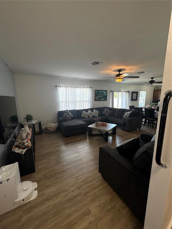 A living room with wood-look flooring, a large sectional sofa, and an open dining area — 5780 LAKESIDE LANDINGS BOULEVARD, WINTER HAVEN, FL