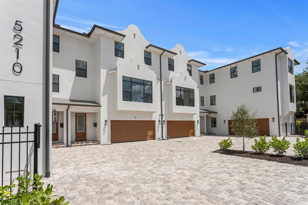 A multi-story white townhouse complex features a paved courtyard, wooden garage doors, and arched gables — 5210 BAYSHORE BOULEVARD UNIT 4, TAMPA, FL