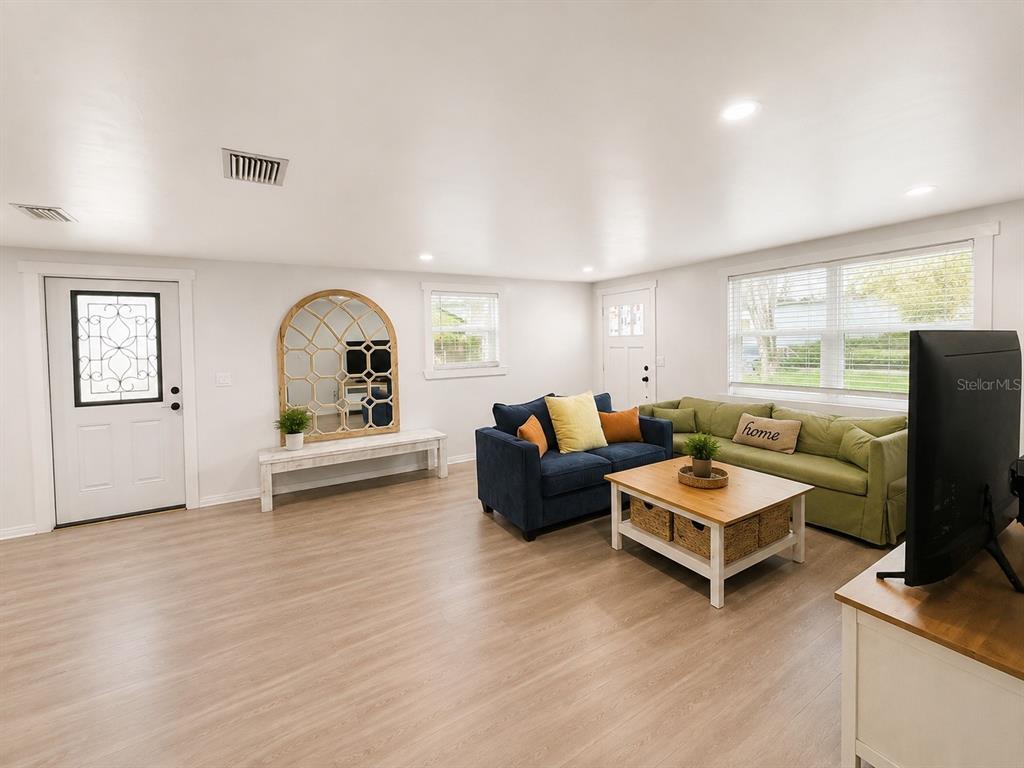 A living room features light wood-look flooring, a blue sofa, a green sofa, and a mirror — 5117 N TALIAFERRO AVENUE, TAMPA, FL