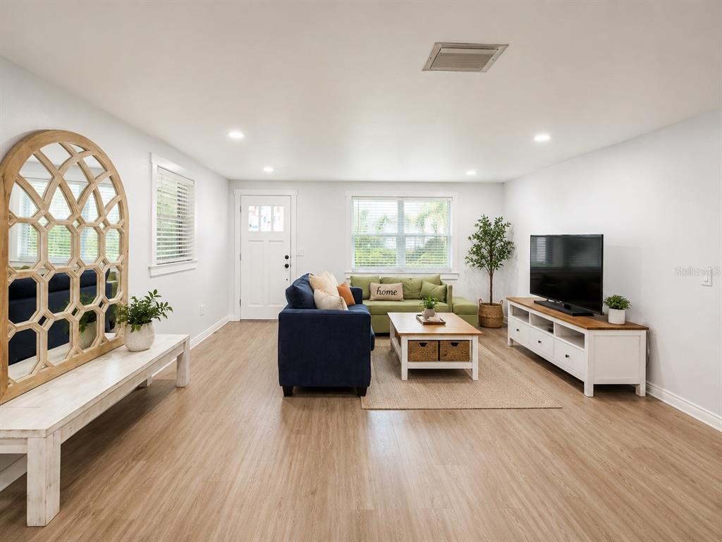 A living room features light wood flooring, a blue sofa, a green sofa, and a television — 5117 N TALIAFERRO AVENUE, TAMPA, FL