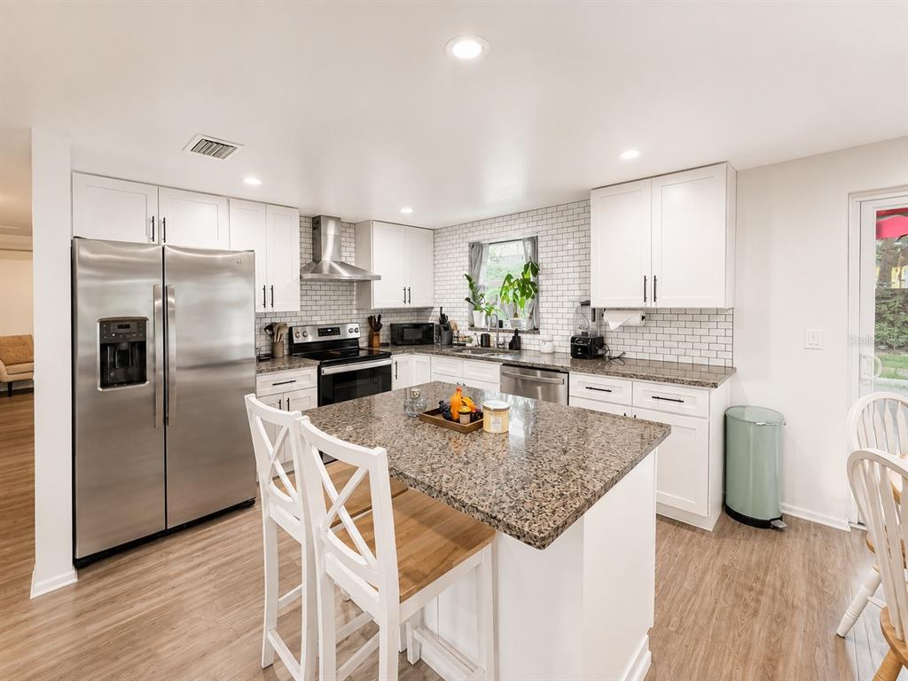 A kitchen features white cabinets, granite countertops, stainless steel appliances, and a central island — 5117 N TALIAFERRO AVENUE, TAMPA, FL