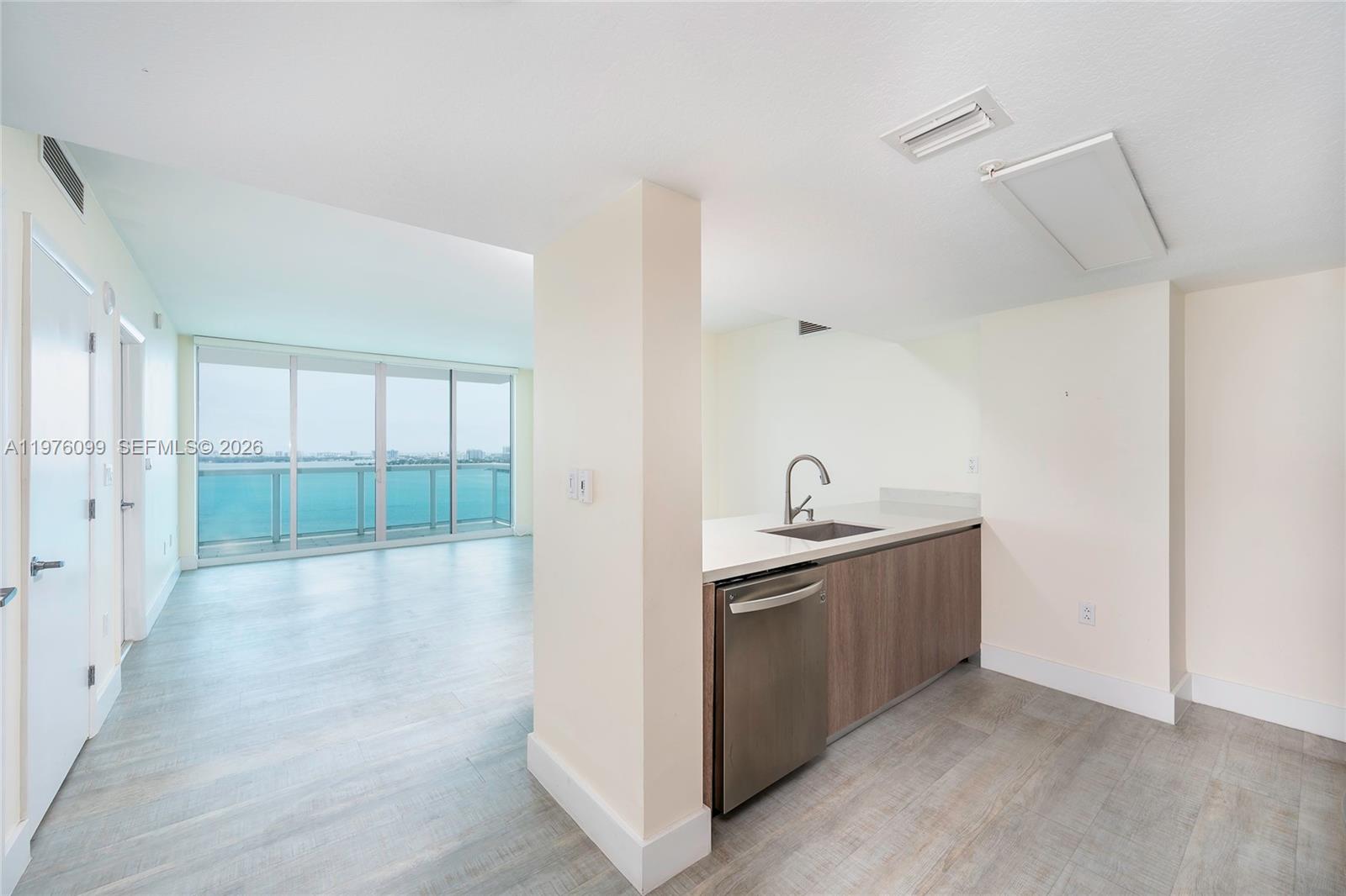 A kitchen area with wood-toned cabinets and a stainless dishwasher overlooks a bright living space — 1800 N Bayshore Dr # 2503, Miami FL 33132, MIAMI, FL