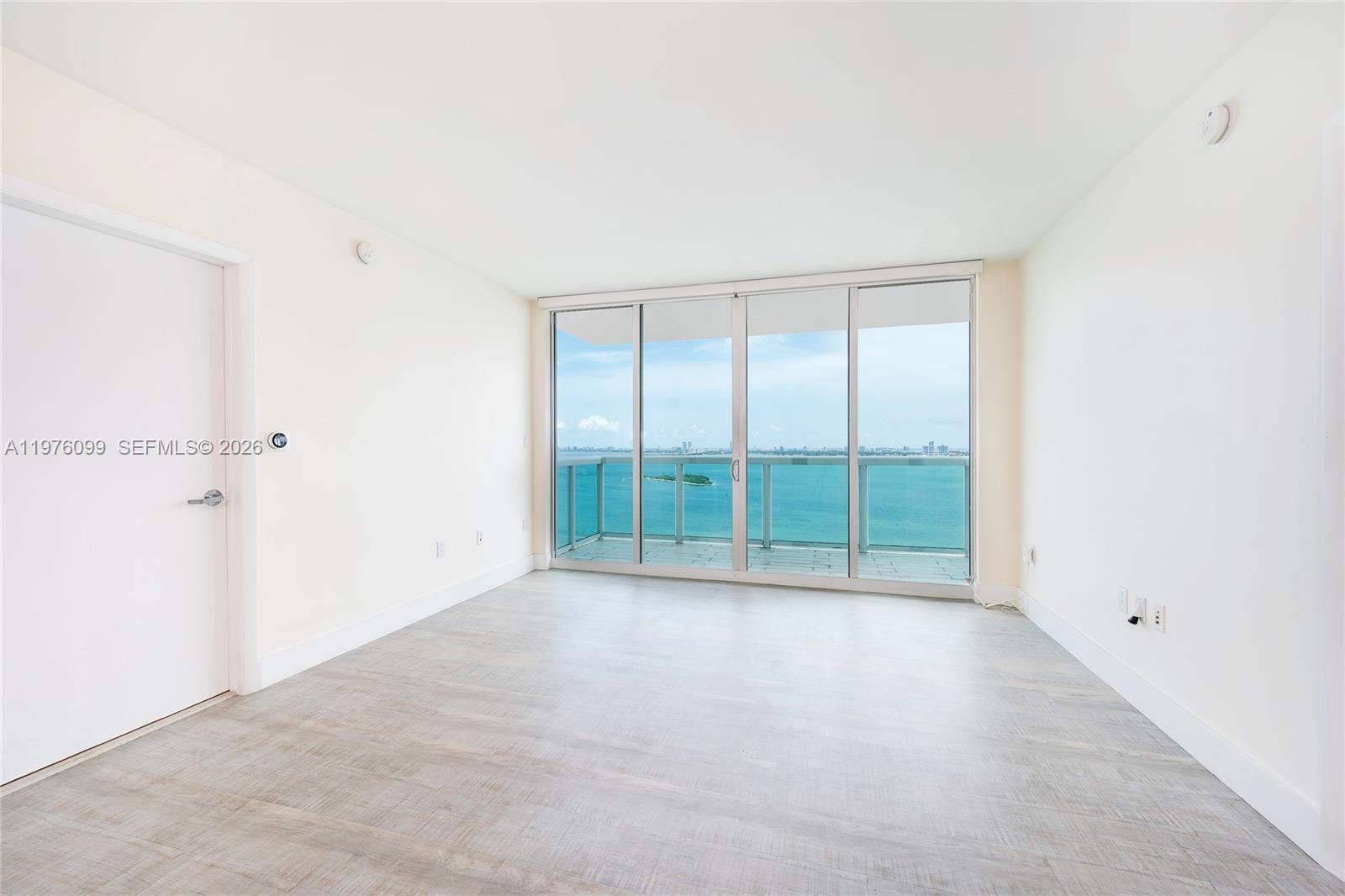 An empty room with light wood-look flooring and a sliding glass door overlooking the ocean — 1800 N Bayshore Dr # 2503, Miami FL 33132, MIAMI, FL