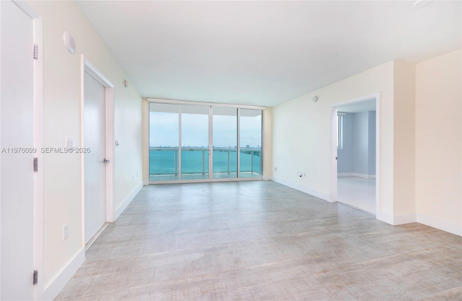 An empty room features light wood-look flooring, white walls, and a balcony overlooking the ocean — 1800 N Bayshore Dr # 2503, Miami FL 33132, MIAMI, FL