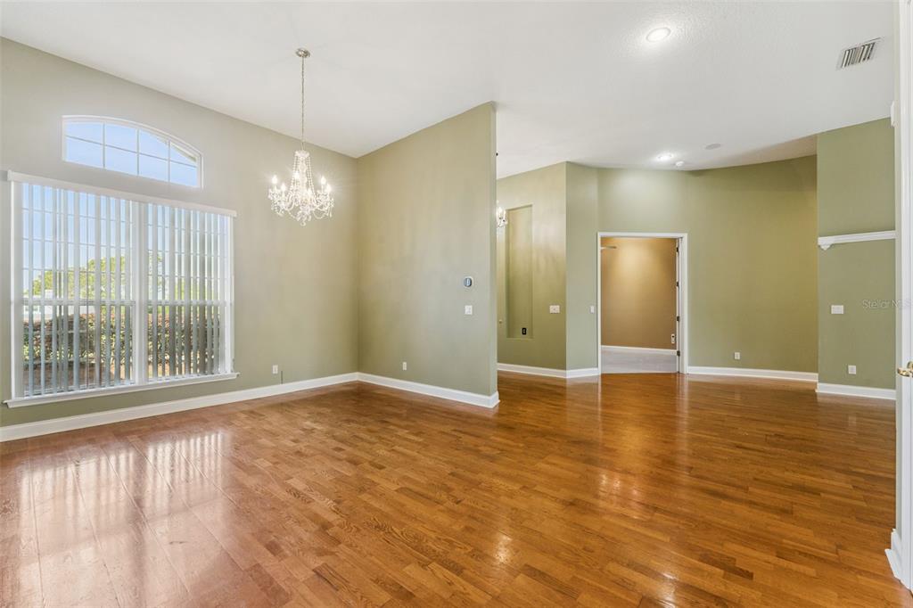 An empty room with hardwood floors, sage green walls, a crystal chandelier, and large windows — 17540 VISTA BELLE COURT, MONTVERDE, FL