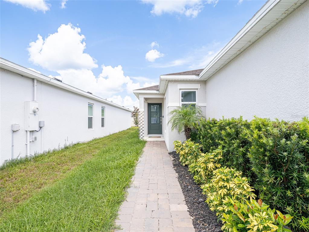 A paved walkway leads to the front entrance of a house with white stucco walls — 2893 SANCTUARY DRIVE, CLERMONT, FL