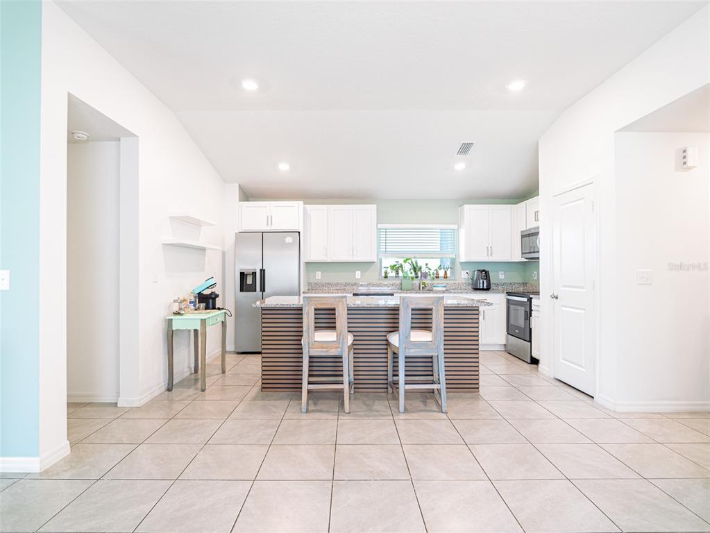 A kitchen features white cabinets, a slatted kitchen island with two chairs, and tile flooring — 2893 SANCTUARY DRIVE, CLERMONT, FL