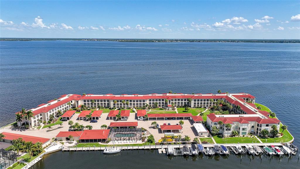 An aerial view shows a large waterfront apartment complex with red roofs and boat slips — 1 COLONY POINT DRIVE UNIT A10, PUNTA GORDA, FL