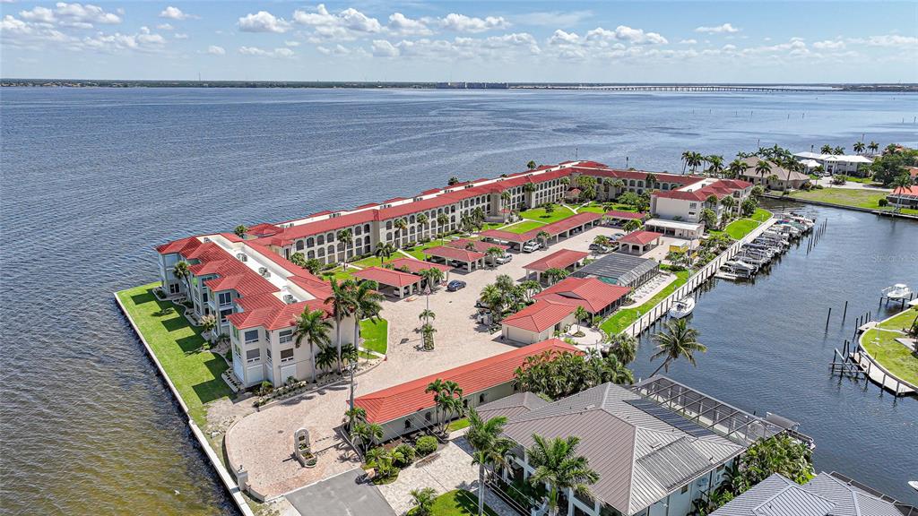 An aerial view shows a multi-story waterfront apartment complex with a pool and boat slips — 1 COLONY POINT DRIVE UNIT A10, PUNTA GORDA, FL