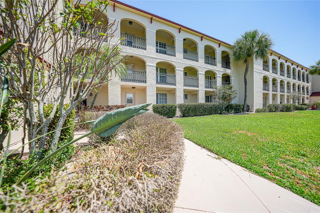 A three-story apartment building features arched balconies and a landscaped lawn with a paved walkway — 1 COLONY POINT DRIVE UNIT A10, PUNTA GORDA, FL