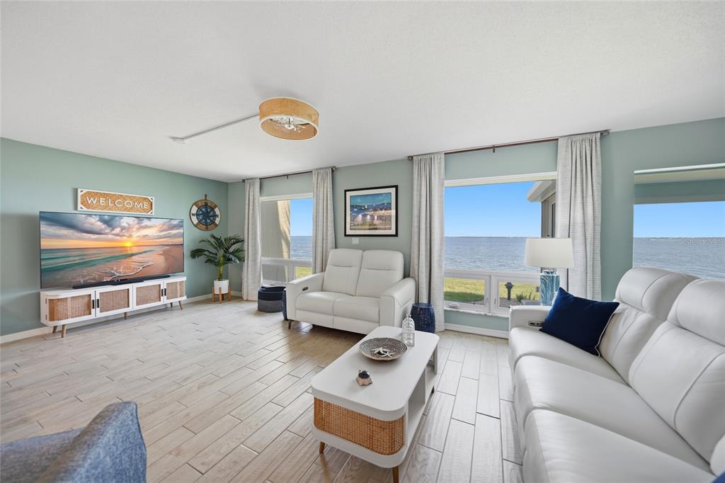 A living room features white leather sofas, a coffee table, and large windows overlooking water — 1 COLONY POINT DRIVE UNIT A10, PUNTA GORDA, FL