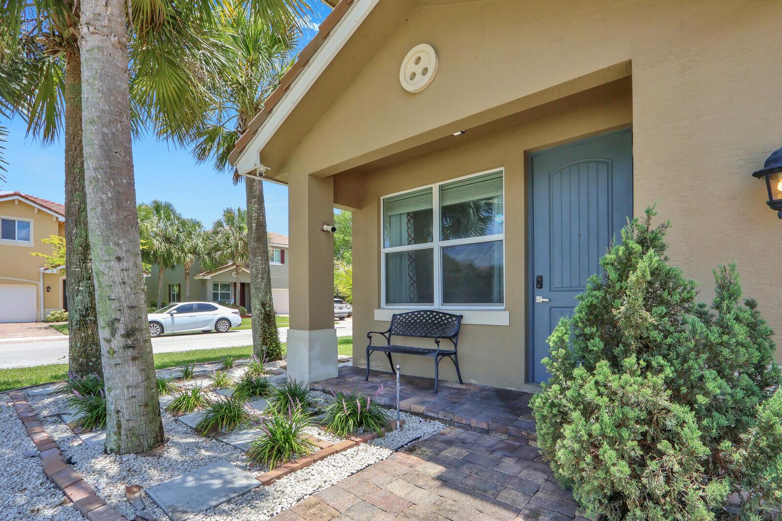 A tan house exterior features a blue front door, a metal bench, and palm trees — 4701 Foxtail Palm Court, FL 33463, FL