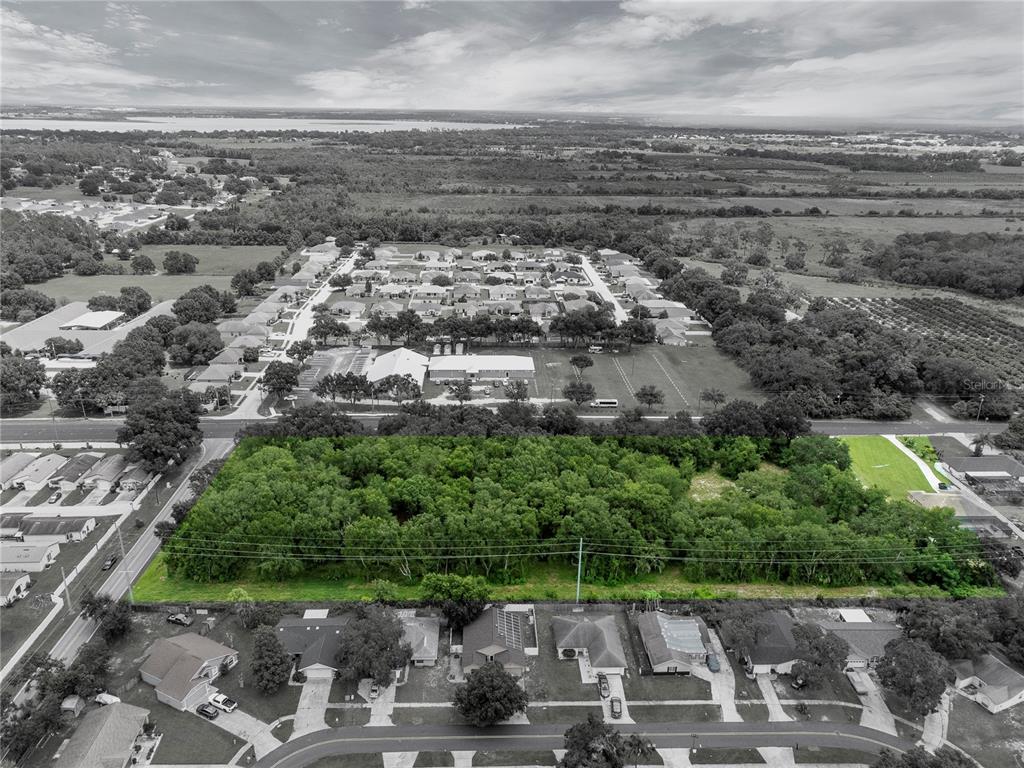 An aerial view shows a rectangular, tree-covered vacant lot bordered by residential streets and houses — 2400 BUCKEYE ROAD NE, WINTER HAVEN, FL