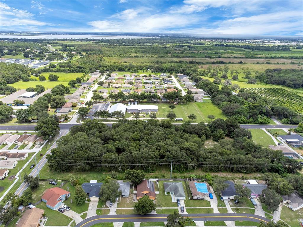 An aerial view shows a wooded lot situated between a residential neighborhood and a large building — 2400 BUCKEYE ROAD NE, WINTER HAVEN, FL