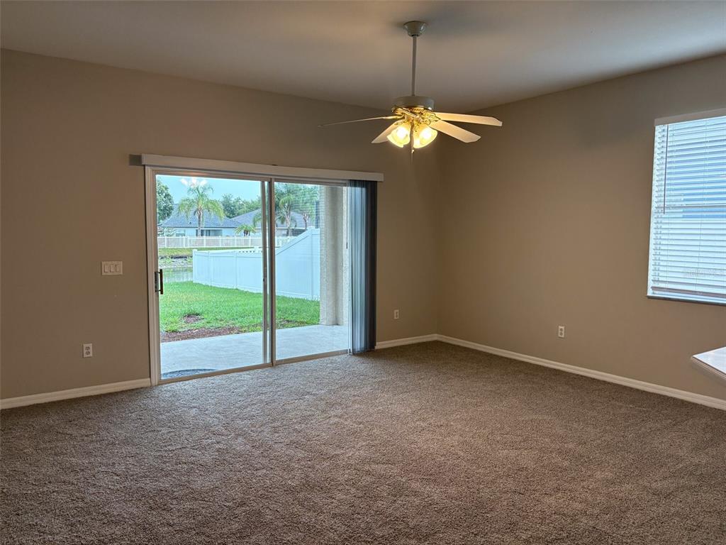An empty living room features beige carpet, a ceiling fan, and sliding glass patio doors — 3922 WASHBURN PLACE, WESLEY CHAPEL, FL