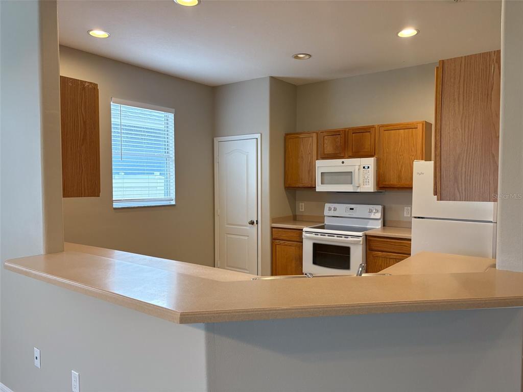 A kitchen with wood cabinets, white appliances, and a breakfast bar overlooking the room — 3922 WASHBURN PLACE, WESLEY CHAPEL, FL