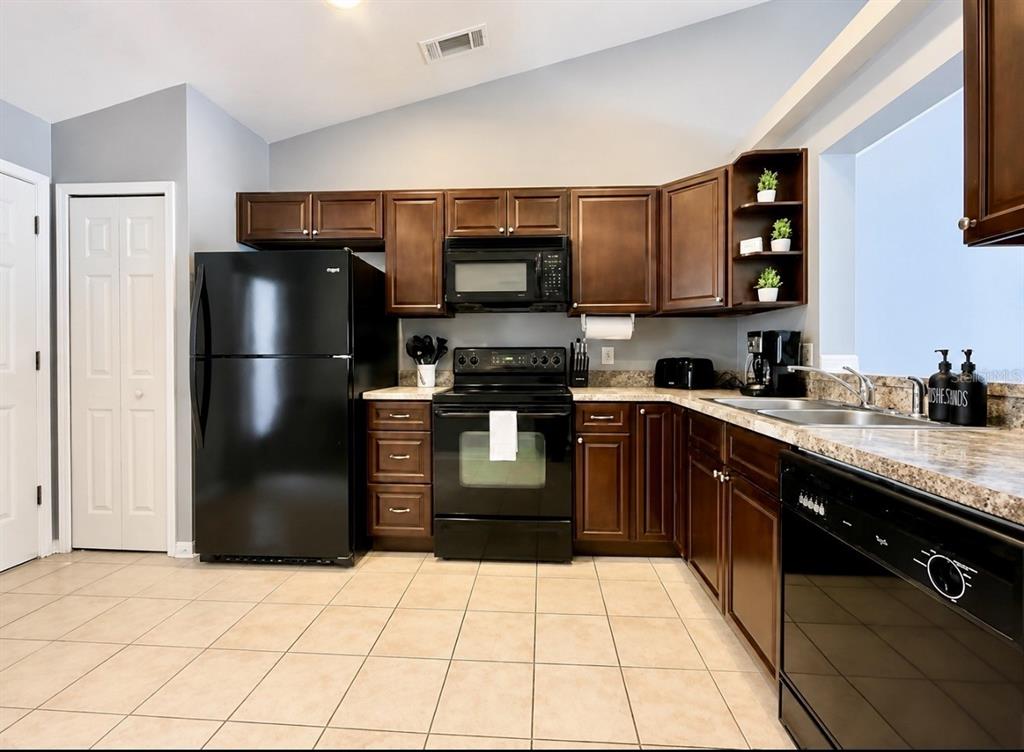 A kitchen features dark wood cabinets, black appliances, granite countertops, and light-colored tile flooring — 142 GLASGOW COURT, DAVENPORT, FL