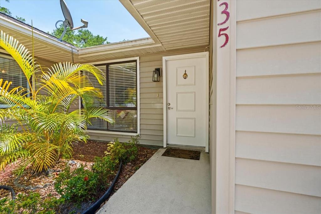 The exterior of a home features a white front door, beige siding, and a palm tree — 16235 BANYAN AVENUE, PORT CHARLOTTE, FL