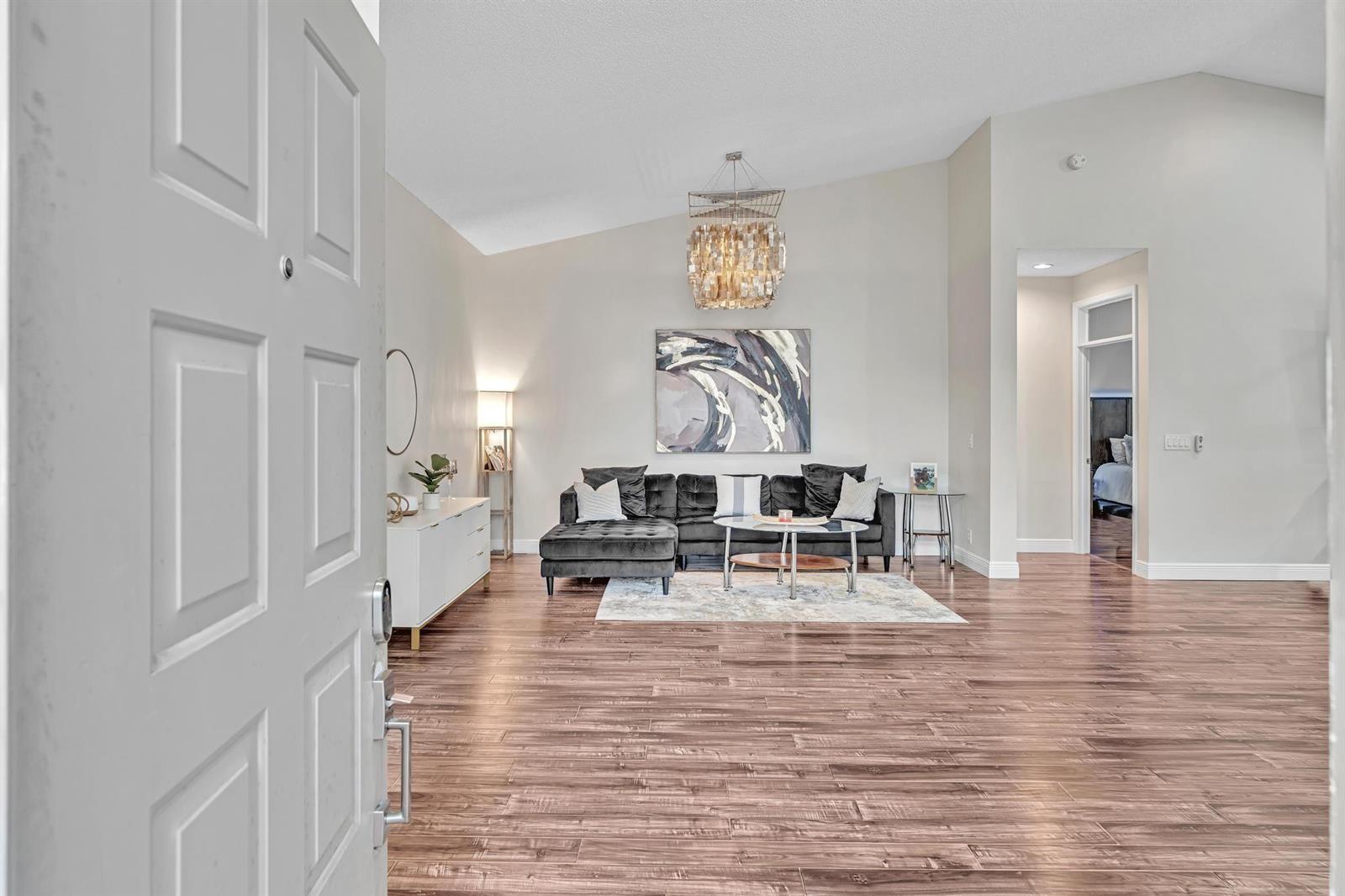 A living room features a dark sectional sofa, a chandelier, and wood-look flooring — 7445 Rockbridge Circle, Lake Worth FL 33467, LAKE WORTH, FL