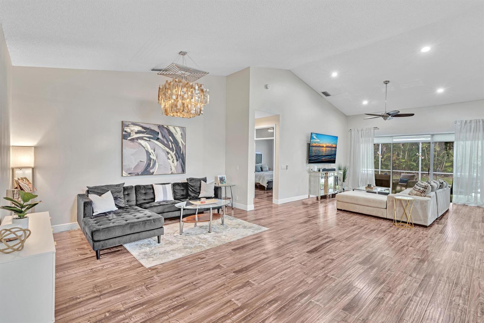 A spacious living room features wood-look tile flooring, two sectional sofas, and a vaulted ceiling — 7445 Rockbridge Circle, Lake Worth FL 33467, LAKE WORTH, FL